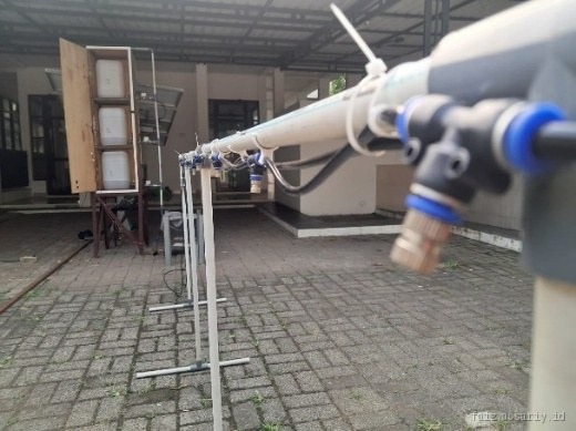 Close view along the spray boom: white pipe with brass misting nozzle fittings spaced at intervals, mounted on white stands.